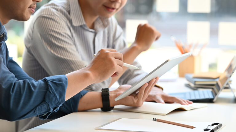 Two men working at a table with a tablet device